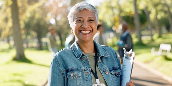 Smiling woman with clipboard outdoors in a sunny park.