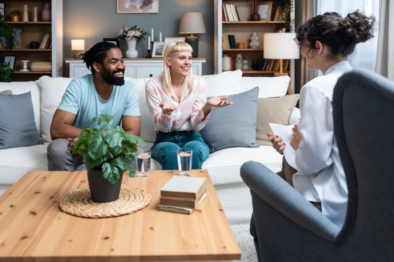 Two people, young diverse couple trying to solve issues in their relationship. Multiracial spouses smiling while talking in front of a therapist in the office. Marital therapy. Family reconciliation.