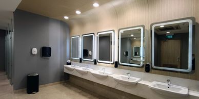 Modern public restroom with illuminated mirrors and multiple sinks.
