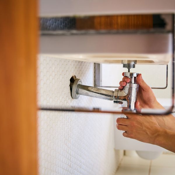 Person repairing a chrome sink pipe under a bathroom sink.