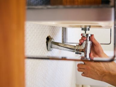 Person repairing a chrome sink pipe under a bathroom sink.
