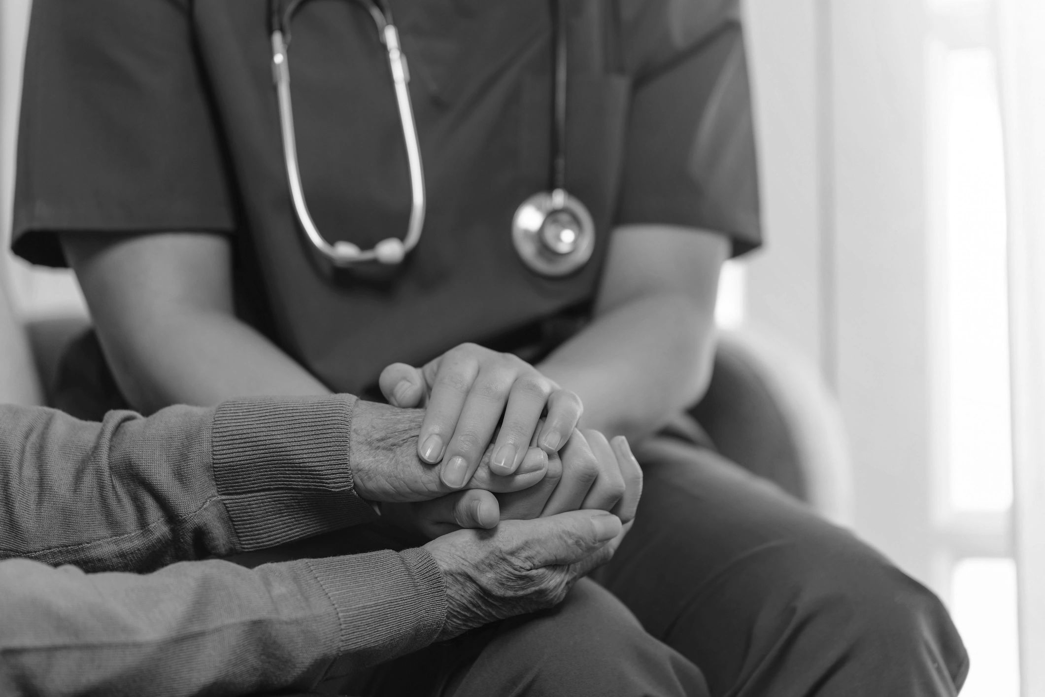 A healthcare worker in blue scrubs holding an elderly person's hands.