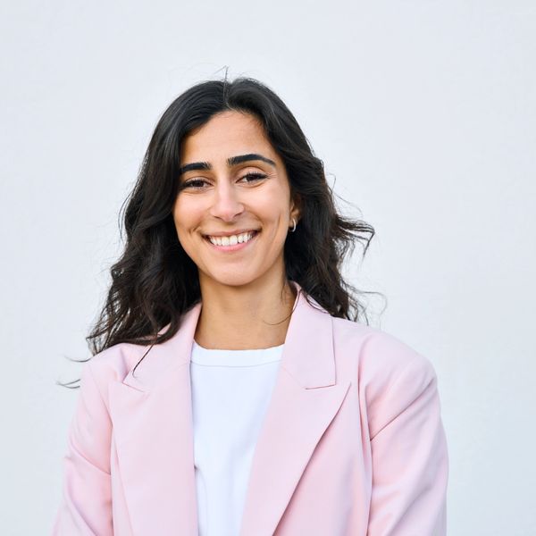 Confident woman smiling in a light pink blazer against a plain background.