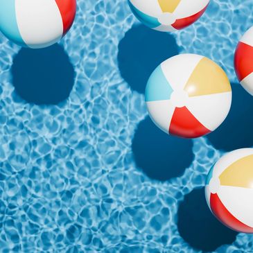 Colorful beach balls floating on clear blue pool water casting shadows.