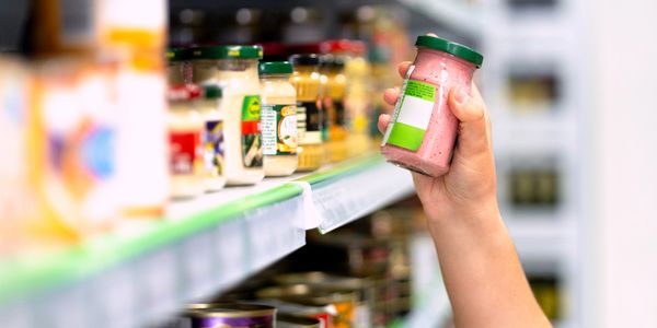 Hand holding a jar of sauce in a grocery store aisle.