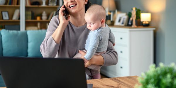 Happy woman working from home while holding her baby and talking on the phone.