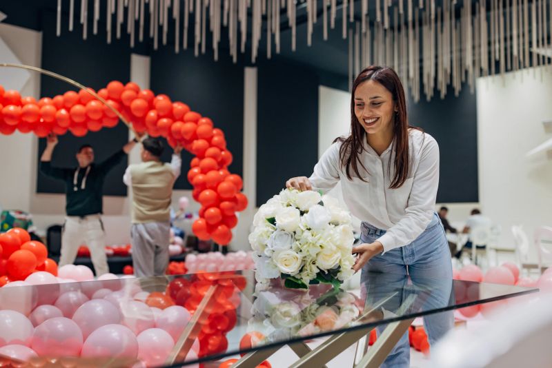 A smiling event organizer places a flower arrangement on the tables in the restaurant. Party decoration, flower arrangements