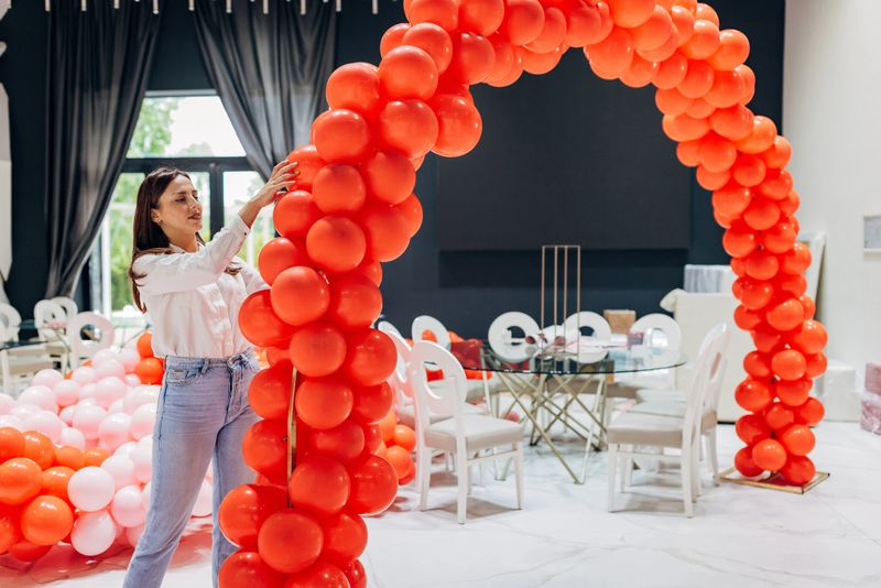 The female decorator decorates the restaurant hall, making a decorative balloon arch