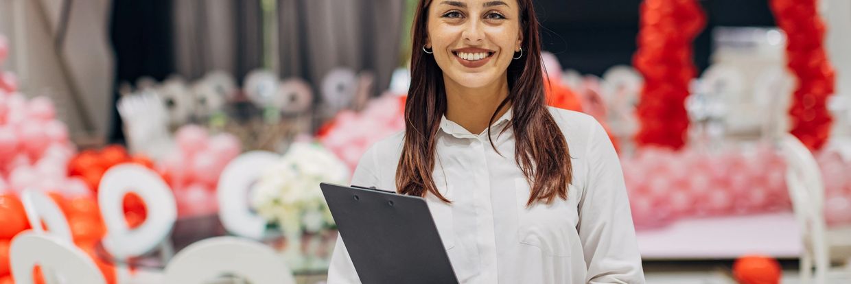 Smiling event planner holding a clipboard in a decorated venue.
