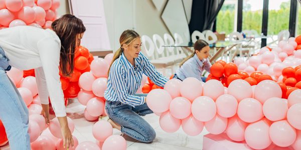 Three women arranging pink and red balloons indoors for decoration.