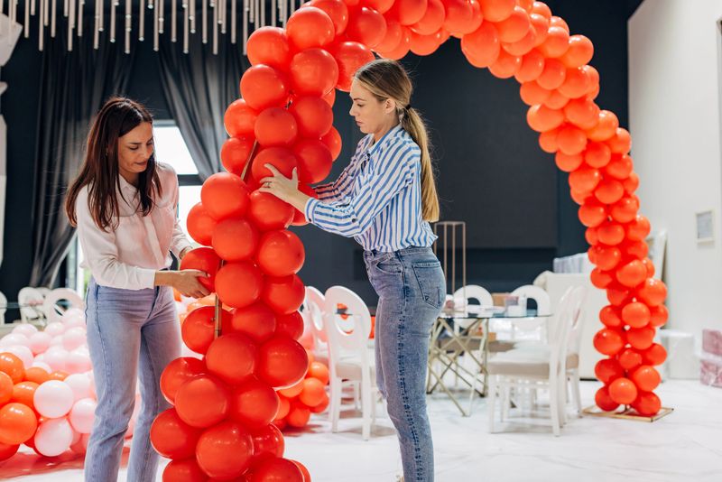 Two female decorators set up a balloon arch as the main decoration in the restaurant hall, for a party