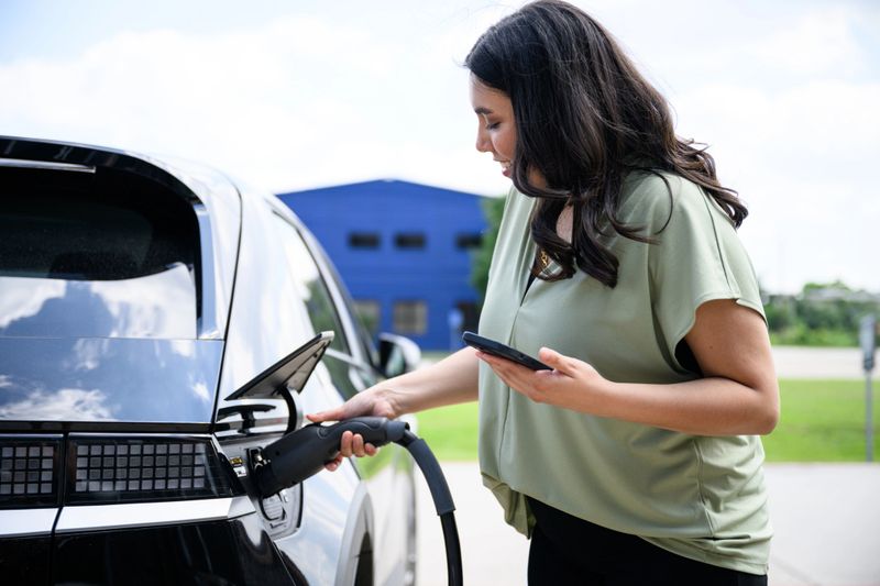 Young woman charging electric vehicle at station using mobile app to buy electricity