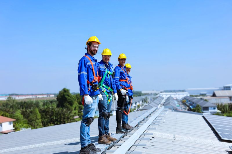 Group of workers stand inline on the factory roof preparing to inspect solar panels.