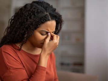 Women with a headache holding her nose and head wearing a burnt orange top