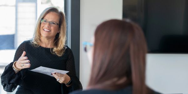 Woman holding paper and talking in an office setting.