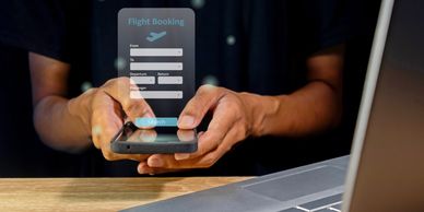 Person booking a flight on a smartphone with a laptop nearby.