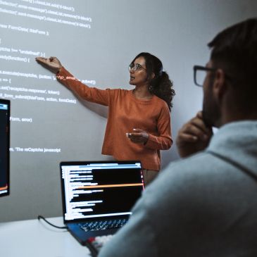 Woman presenting code on a screen to a colleague in an office.
