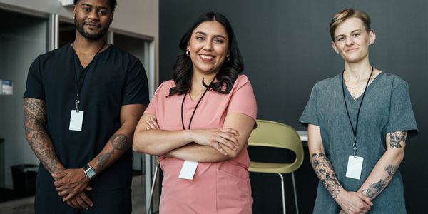 Three healthcare professionals posing confidently, wearing scrubs and ID badges.