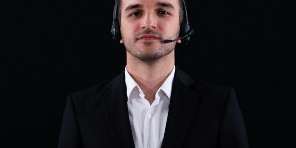 Man in a black suit wearing a headset against a black background.