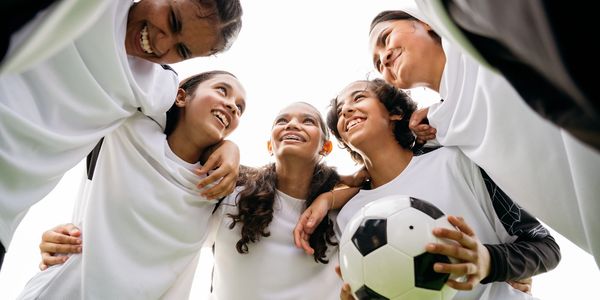 Girls soccer team huddles together smiling with a soccer ball in hand.