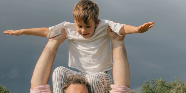 Father lifting his son on his shoulders with arms outstretched outdoors. He got advice where to holiday with kids.