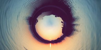 Circular panorama of a sunset over water with silhouetted trees.