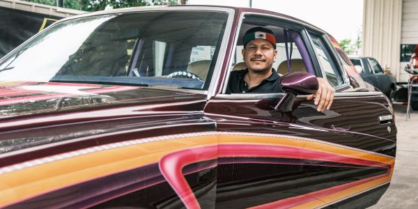 Man smiling inside a customized car with vibrant paintwork.