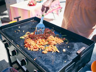 Cooking fried rice on an outdoor griddle with a spatula.