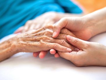 A young hand gently holding an elderly hand, symbolizing care and support.