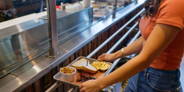 Person holding a tray with food in a cafeteria.