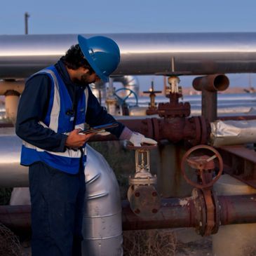 Worker inspecting industrial pipeline valve with tablet in hand.