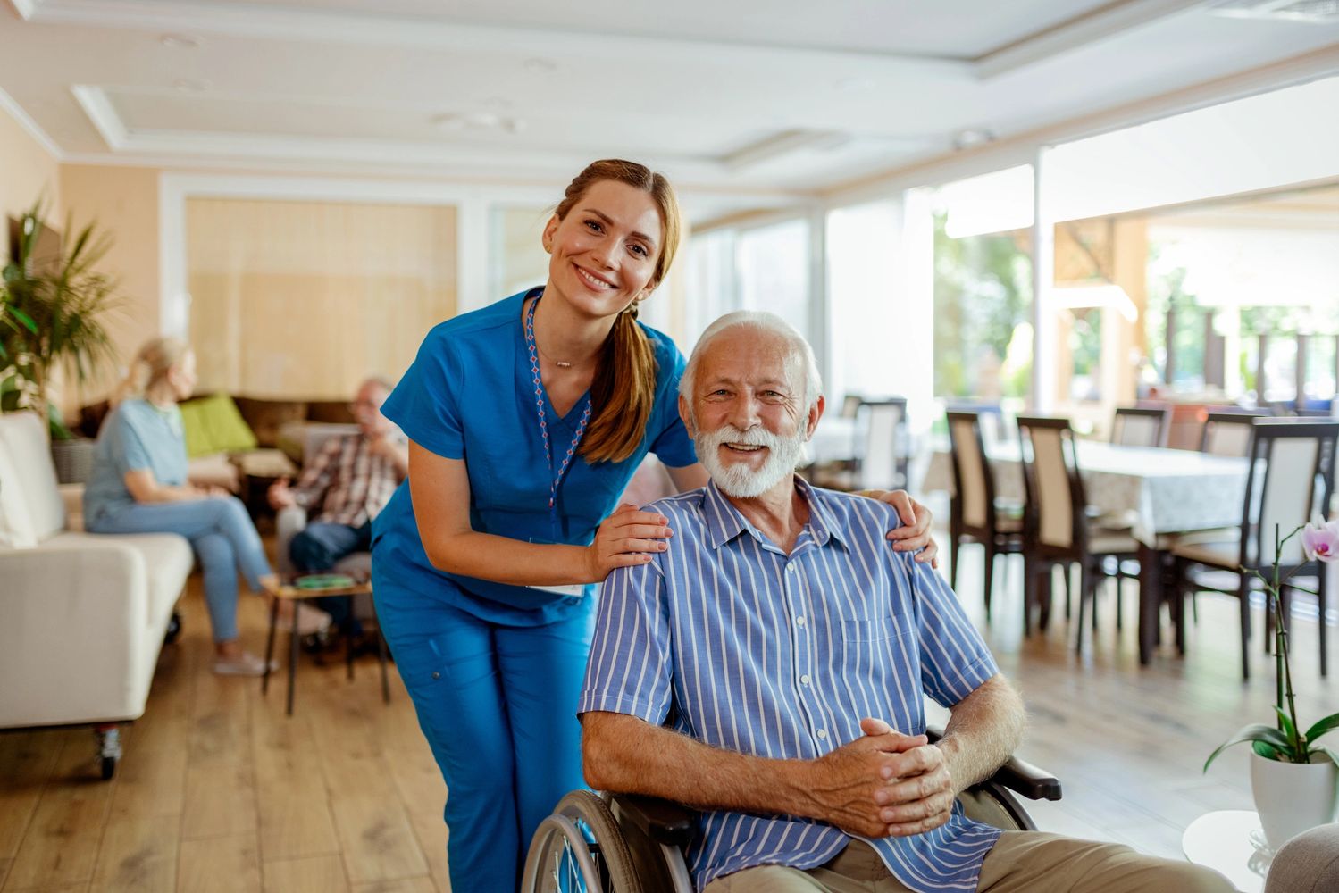 Nurse smiling with elderly man in wheelchair at care home.