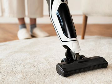 Person vacuuming a light carpet with a modern vacuum cleaner.