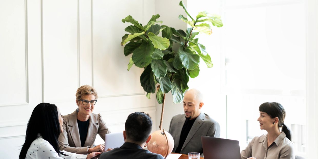 Five professionals engaged in a meeting around a table with laptops and a globe.