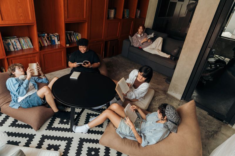 Gen Z travelers relaxing with books in a cozy hostel lounge, enjoying leisure time and the comfortable atmosphere of their accommodation.