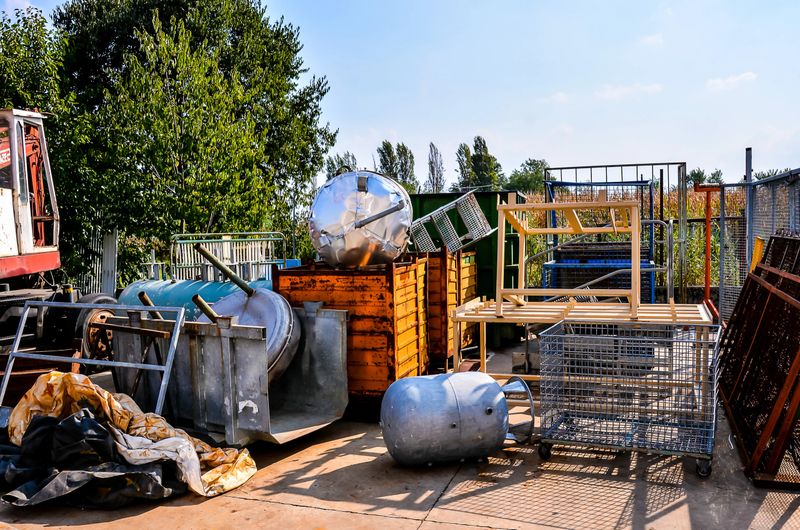 A pile of junk and debris, including a large metal container, is scattered across a dirt field. The scene is chaotic and disorganized, with no clear purpose or destination for the items