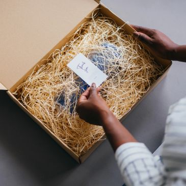 Person holding a card inside a box filled with packing straw.