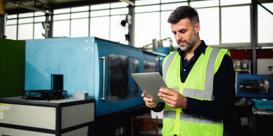 Man in high-visibility vest using a tablet in a factory.