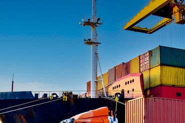 Orange truck transporting cargo containers at a busy port near a large ship.