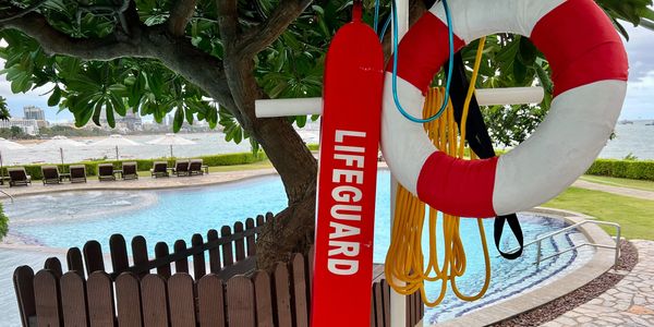 Lifeguard equipment by a poolside with ocean view and lounge chairs.