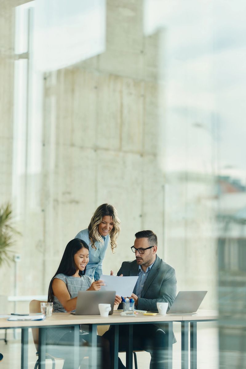 Team of happy entrepreneurs cooperating while working on business documents in the office. The view is through glass. Copy space.