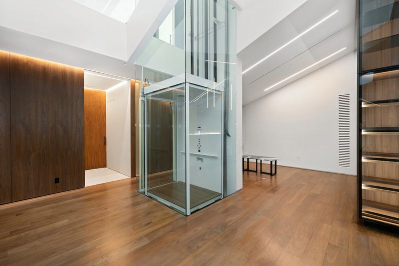 An empty room with wooden floors and a transparent elevator system