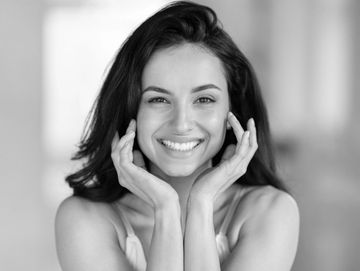 A joyful woman smiling brightly with hands framing her face.
