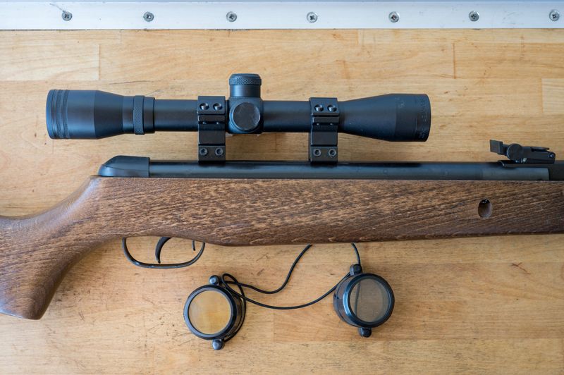 Detail of a light precision air rifle with optical sight on a wooden table. It is a 4.5mm caliber rifle for hunting pigeons.