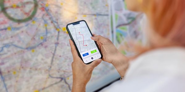 Person holding smartphone with a route map, looking at a large city map.
