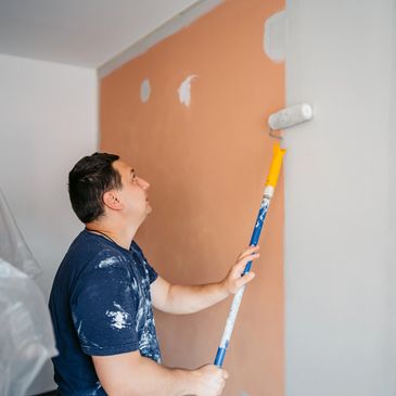 Man painting a wall white with a roller.