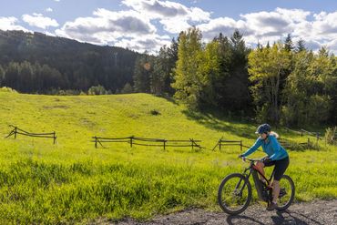 Person biking near a green field and forested hills.