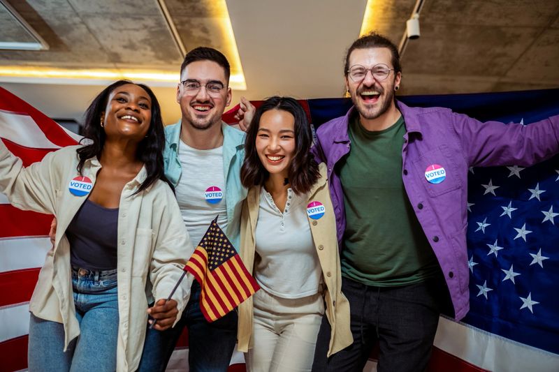 Diverse group of people stands proudly together, displaying an "I Voted" sticker on their clothing
