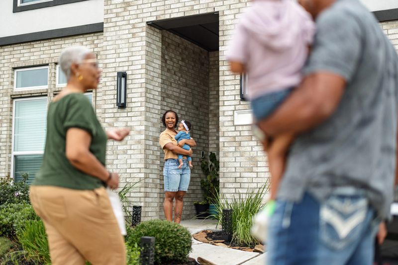 A cheerful multiracial family gathers at the entrance of a modern home. A mother holding her baby warmly greets her father and grandmother, symbolizing love, connection, and togetherness.