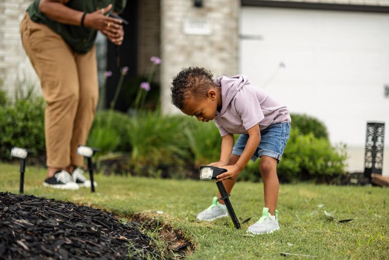 Multiethnic grandmother and grandson install solar-powered LED panels in their yard, emphasizing sustainability and family bonding. The child intently places a panel in the ground while the grandmother assists.
